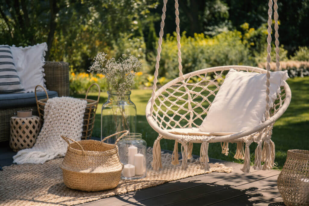 A hanging chair hovers above a deck, with baskets, pillows and glass jars placed nearby.