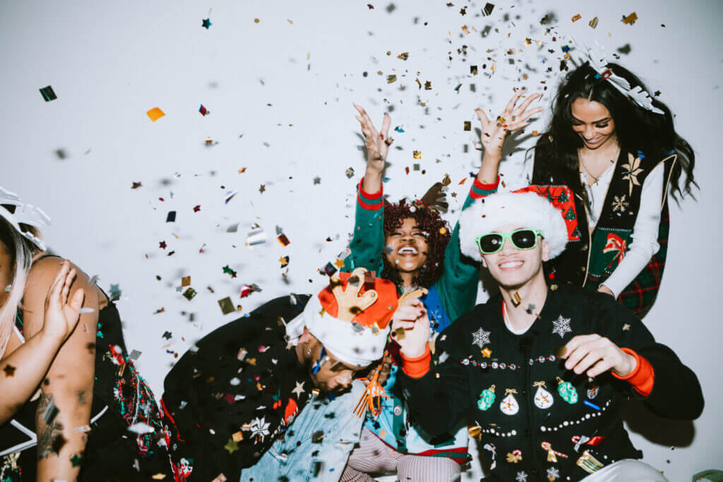 A group of friends celebrate with confetti and Christmas sweaters.