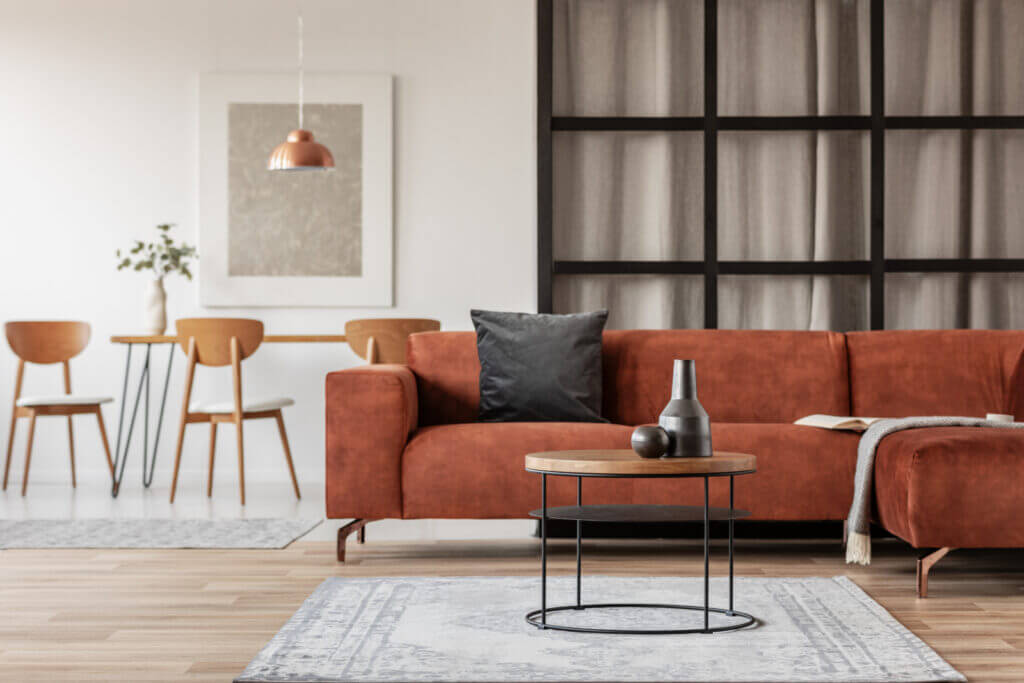 A rustic red-colored couch sits in a peaceful room near a rug, with several pieces of wood-toned furniture in the vicinity.