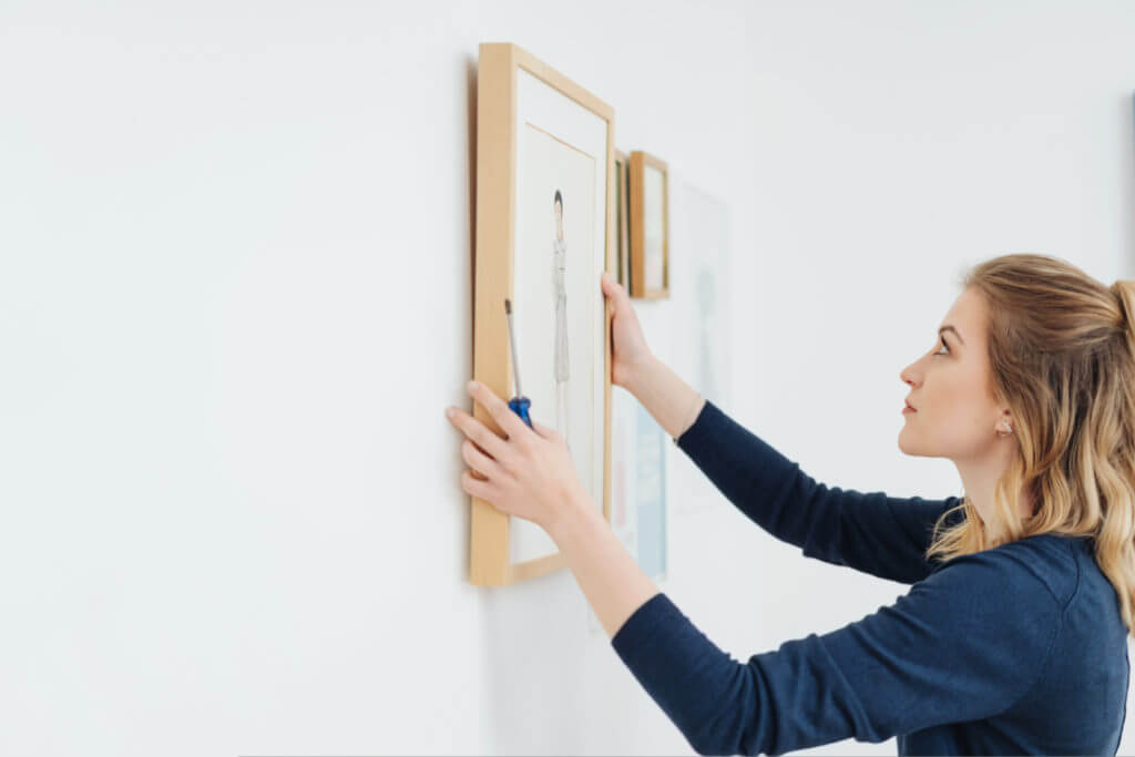 A woman carefully hangs a piece of artwork on the wall.