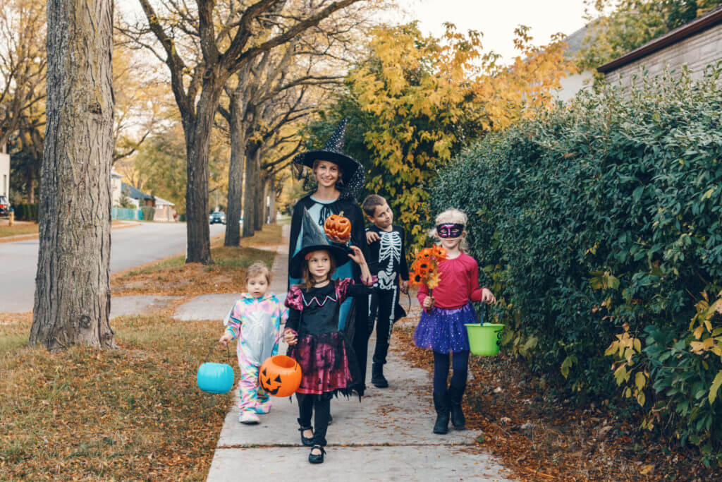 A woman and her four children walk down a sidewalk on Halloween, each wearing a fun costume.