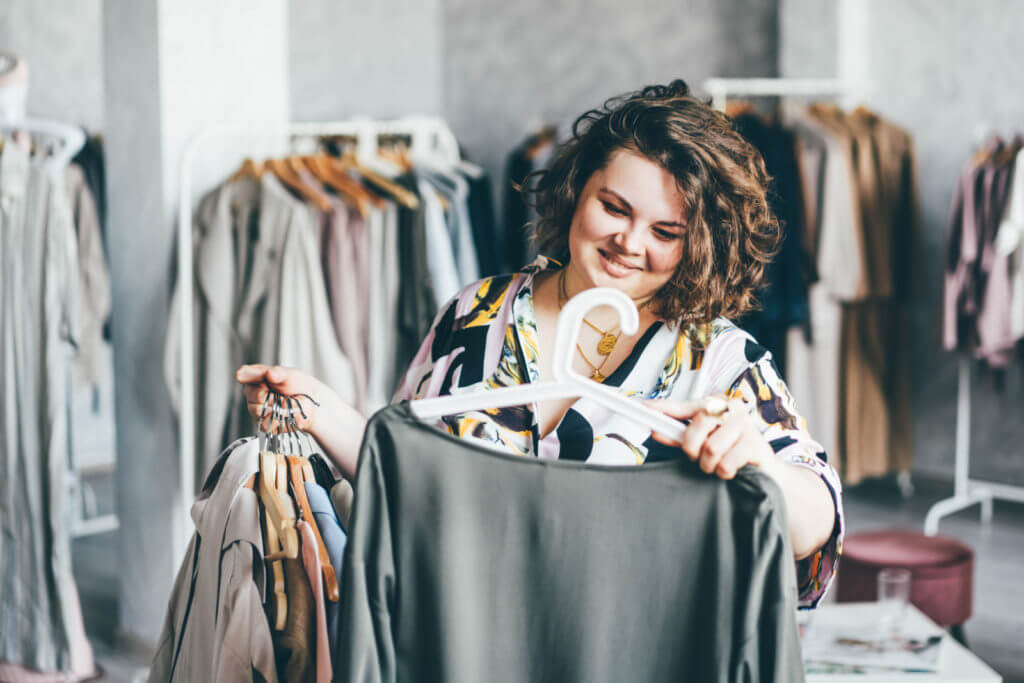 A woman holds out a shirt in front of her to inspect it, while holding a bunch of shirts in her other hand.