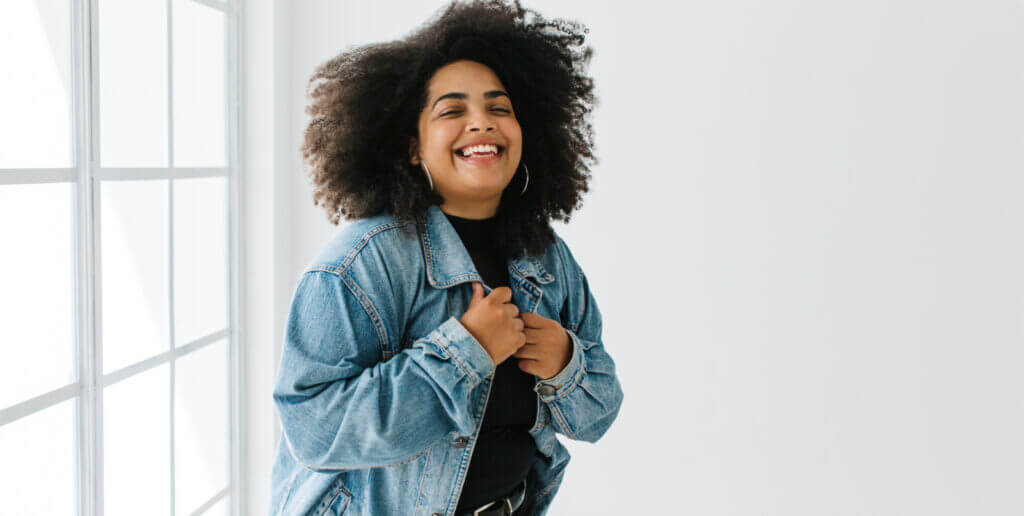 A woman smiles toward the camera while wearing a jean jacket over a black shirt.