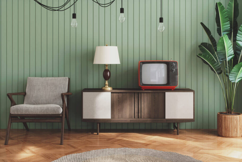 A room is shown with a green beadboard wall, a mid-century modern TV stand and other tasteful decorations.