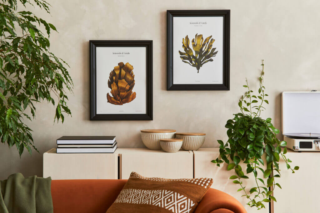 A wall is pictured behind a couch, featuring a shallow cabinet, several houseplants and some artwork hanging up.