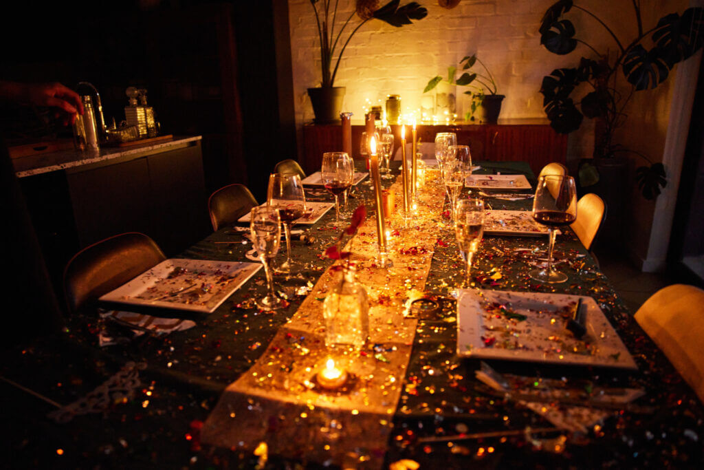 A dining room table is scattered with confetti and candles, contrasting with a dark tablecloth.