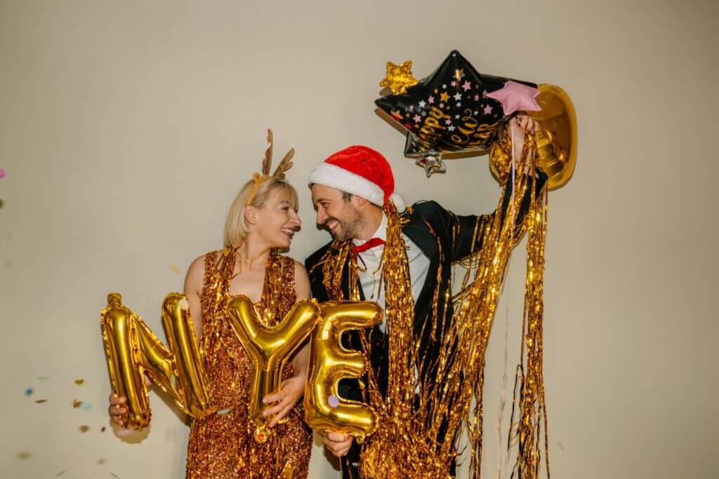 A man and woman hold up various New Year's balloons while celebrating.