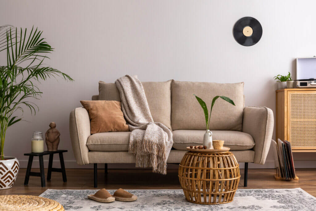 A picture of a warm-colored couch with slippers in front of it, a rug, and several wood-toned decor pieces nearby.