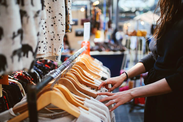 A closeup picture of a woman sorting through a rack of clothes.