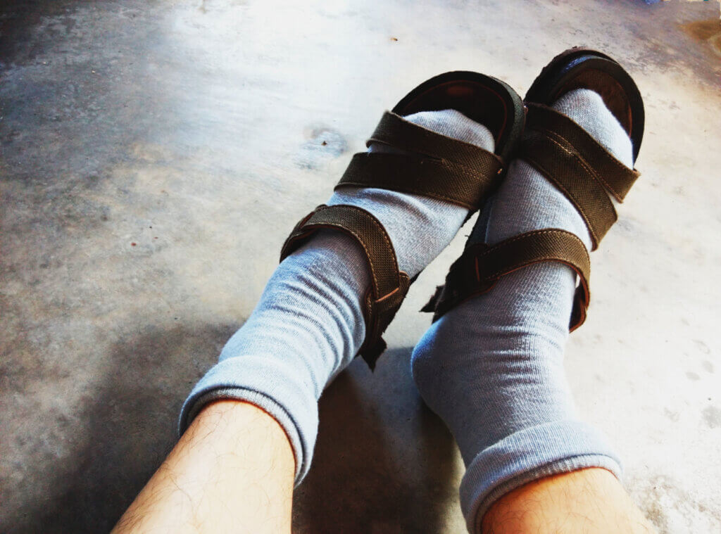 A person's feet are shown, wearing gray socks and brown sandals.