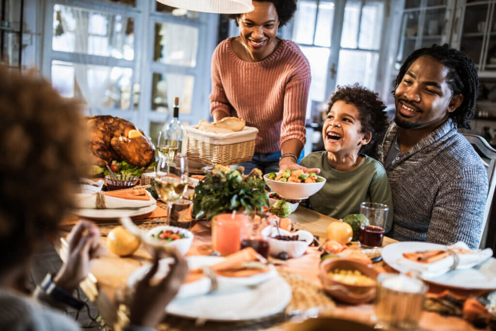 A family laughs around a table as food is passed around.