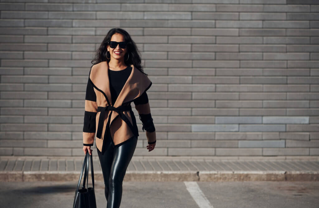 A woman is pictured walking toward the camera wearing a stylish jacket and faux leather pants.